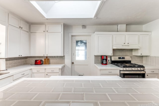 kitchen with tile counters, a skylight, gas stove, white cabinets, and backsplash