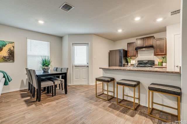 kitchen with light stone counters, fridge, light wood-type flooring, a breakfast bar area, and range