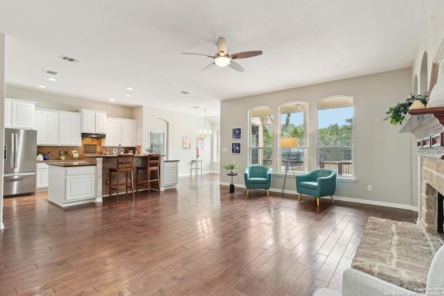 interior space featuring recessed lighting, a fireplace with raised hearth, dark wood-type flooring, baseboards, and ceiling fan with notable chandelier