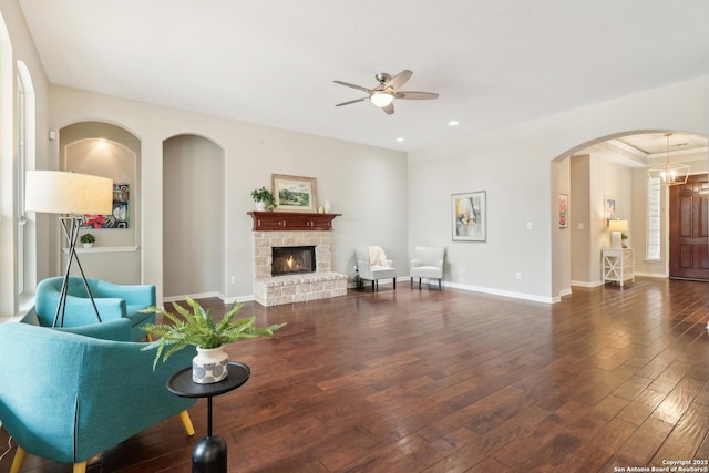 living area featuring arched walkways, a fireplace, wood-type flooring, ceiling fan, and baseboards