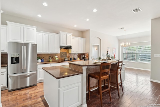 kitchen featuring an island with sink, a notable chandelier, white cabinets, and stainless steel refrigerator with ice dispenser