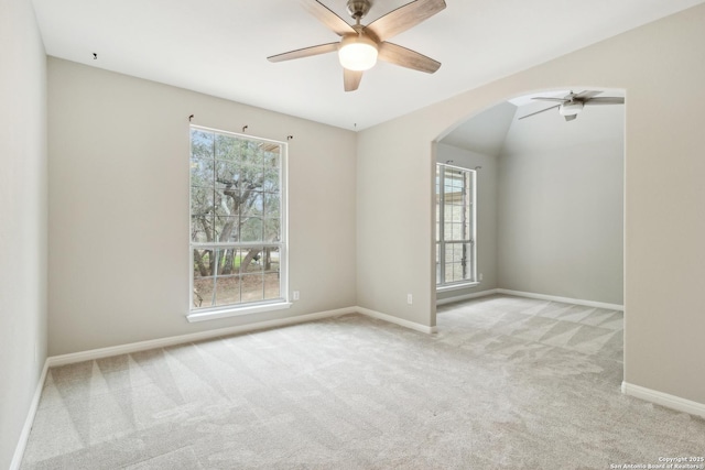 carpeted empty room featuring baseboards, vaulted ceiling, arched walkways, and ceiling fan