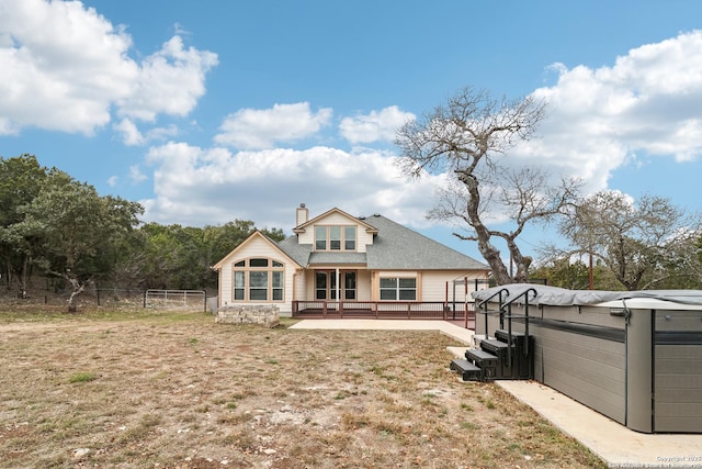 rear view of house featuring a jacuzzi, a chimney, roof with shingles, fence, and a wooden deck