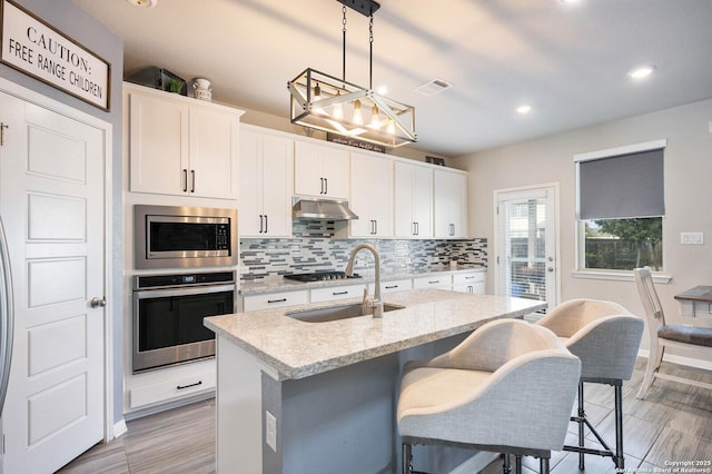 kitchen featuring sink, white cabinets, hanging light fixtures, a kitchen island with sink, and appliances with stainless steel finishes