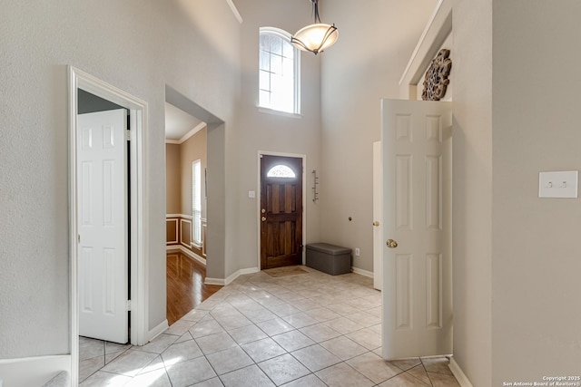 foyer with a towering ceiling, ornamental molding, and light tile patterned floors