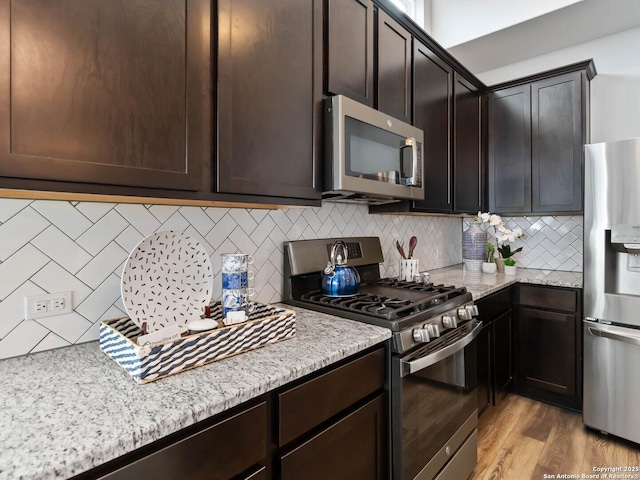 kitchen with appliances with stainless steel finishes, light stone countertops, decorative backsplash, and dark brown cabinetry