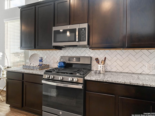 kitchen with light stone countertops, dark brown cabinets, and appliances with stainless steel finishes