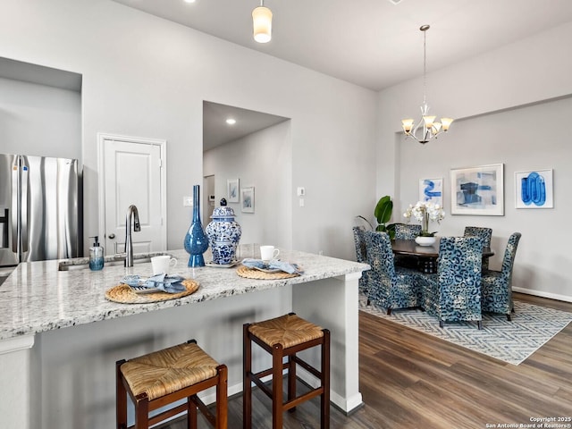 kitchen featuring stainless steel fridge with ice dispenser, a notable chandelier, dark hardwood / wood-style flooring, a kitchen bar, and decorative light fixtures