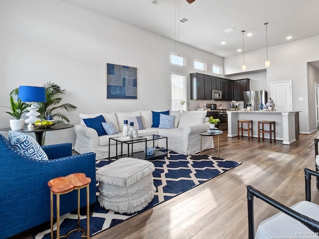 living room featuring a high ceiling, light wood-type flooring, and ceiling fan