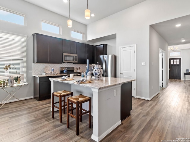 kitchen featuring light stone countertops, pendant lighting, a kitchen island with sink, appliances with stainless steel finishes, and a kitchen breakfast bar