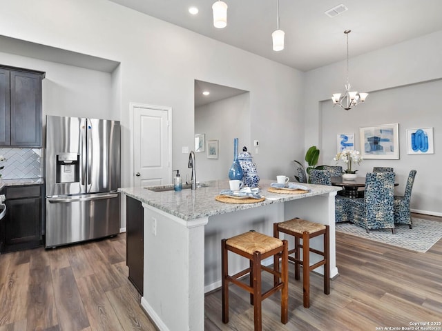 kitchen with a kitchen island with sink, stainless steel fridge with ice dispenser, light stone countertops, a kitchen bar, and sink