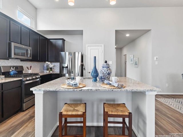 kitchen with stainless steel appliances, a kitchen island with sink, backsplash, and a kitchen bar