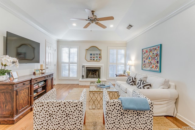 living room with ceiling fan, a tray ceiling, crown molding, and light hardwood / wood-style flooring