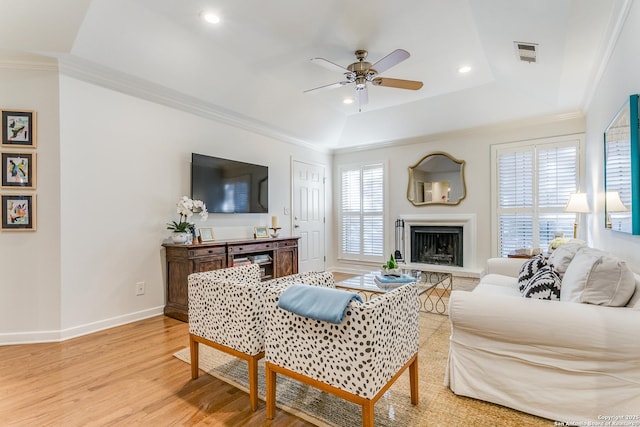 living room with a raised ceiling, ceiling fan, light wood-type flooring, and crown molding