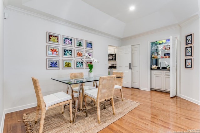 dining space featuring ornamental molding, light hardwood / wood-style flooring, and a raised ceiling