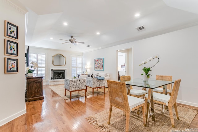 dining space with light wood-type flooring, a raised ceiling, ceiling fan, and crown molding