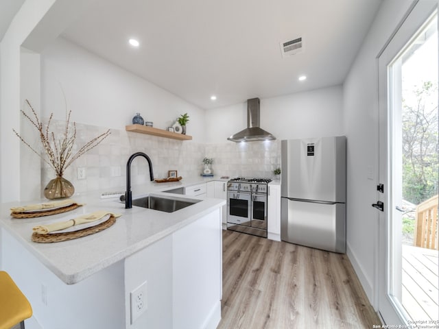 kitchen with appliances with stainless steel finishes, white cabinets, wall chimney range hood, backsplash, and sink