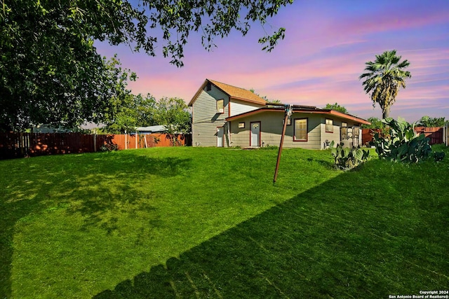 back house at dusk featuring a lawn