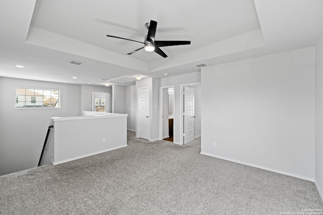 spare room featuring a raised ceiling, light colored carpet, and ceiling fan