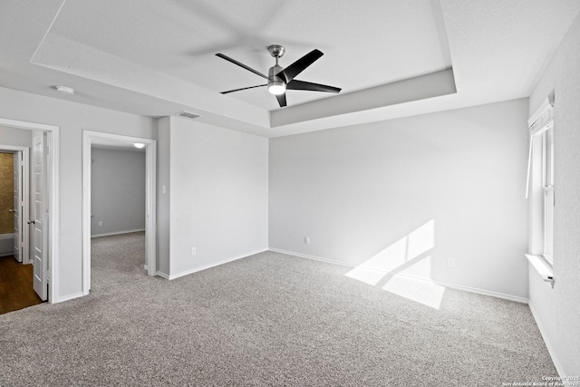 unfurnished room with a raised ceiling, carpet floors, ceiling fan, and plenty of natural light