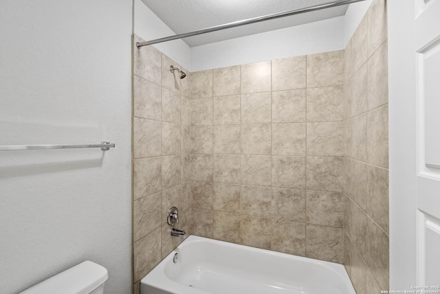 bathroom featuring a textured ceiling, tiled shower / bath combo, and toilet