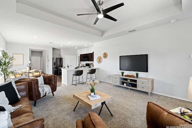 carpeted living room featuring a raised ceiling and ceiling fan