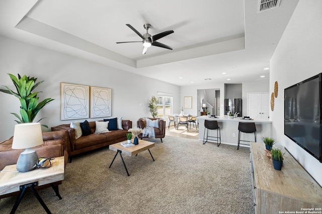 living room with ceiling fan, a tray ceiling, and carpet