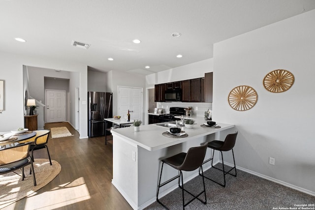 kitchen with kitchen peninsula, a kitchen breakfast bar, black appliances, backsplash, and dark brown cabinets