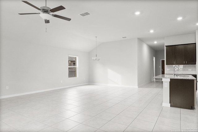 unfurnished living room featuring ceiling fan with notable chandelier, light tile patterned flooring, sink, and vaulted ceiling