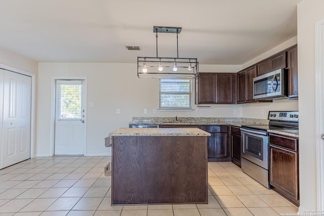 kitchen featuring appliances with stainless steel finishes, light stone counters, a kitchen island, dark brown cabinetry, and decorative light fixtures