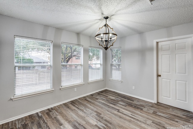 unfurnished dining area featuring a textured ceiling, an inviting chandelier, and wood-type flooring