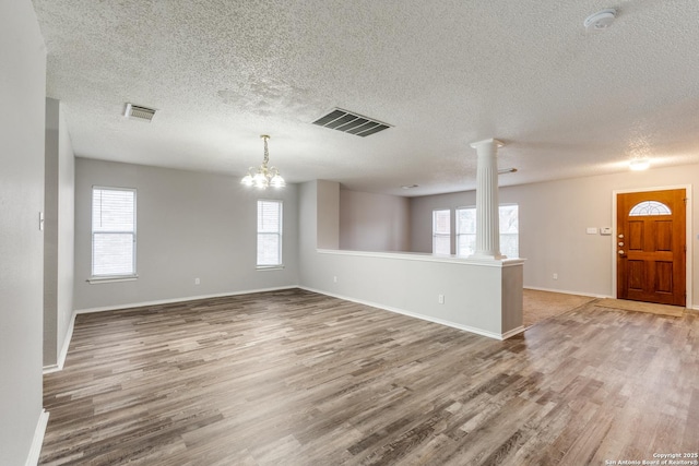 unfurnished room featuring decorative columns, hardwood / wood-style floors, a textured ceiling, and an inviting chandelier