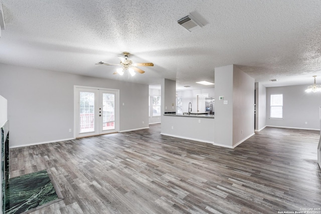 unfurnished living room featuring a healthy amount of sunlight, french doors, sink, and ceiling fan with notable chandelier