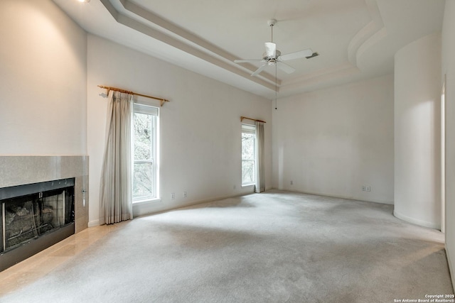 unfurnished living room with a raised ceiling, a tiled fireplace, ceiling fan, and light carpet