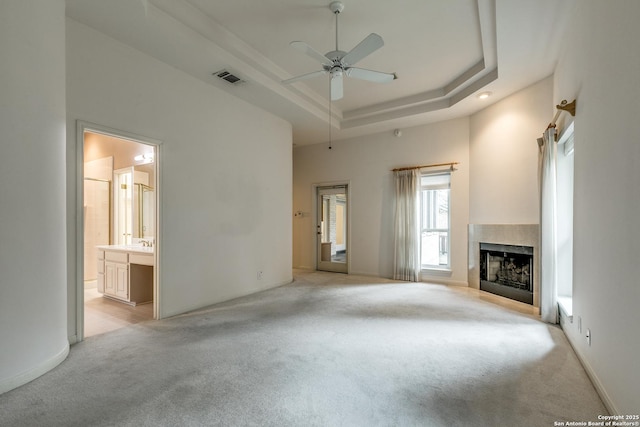 unfurnished living room with a raised ceiling, ceiling fan, and light carpet