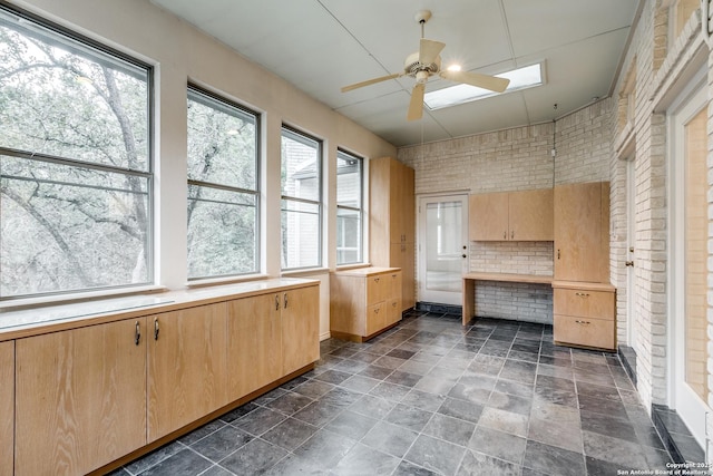 interior space featuring ceiling fan and brick wall