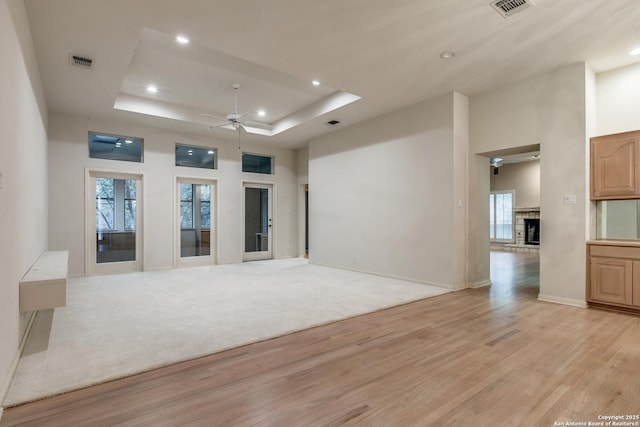 empty room featuring light hardwood / wood-style floors, ceiling fan, and a tray ceiling