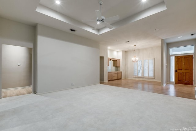 unfurnished living room featuring ceiling fan with notable chandelier, light colored carpet, and a tray ceiling