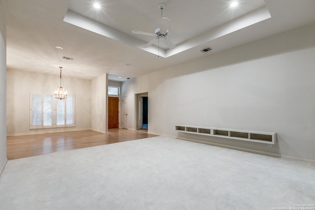 carpeted spare room featuring ceiling fan with notable chandelier and a raised ceiling