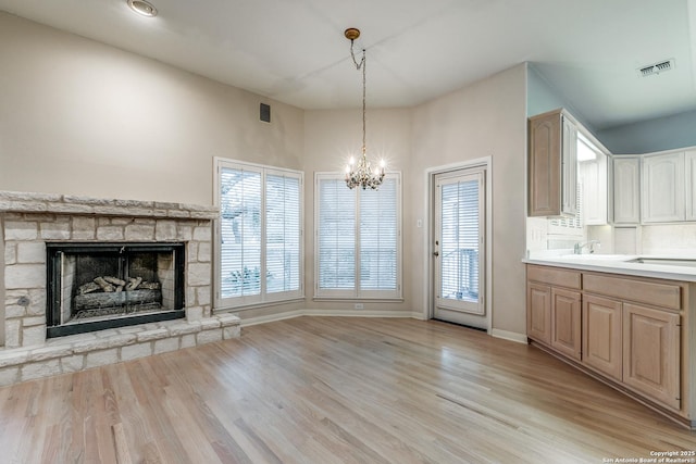 kitchen featuring a stone fireplace, light hardwood / wood-style floors, light brown cabinets, sink, and decorative light fixtures