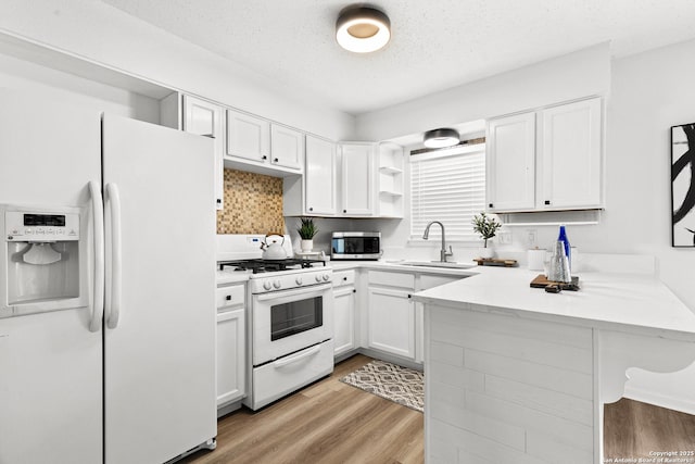 kitchen with white appliances, kitchen peninsula, a textured ceiling, and white cabinetry