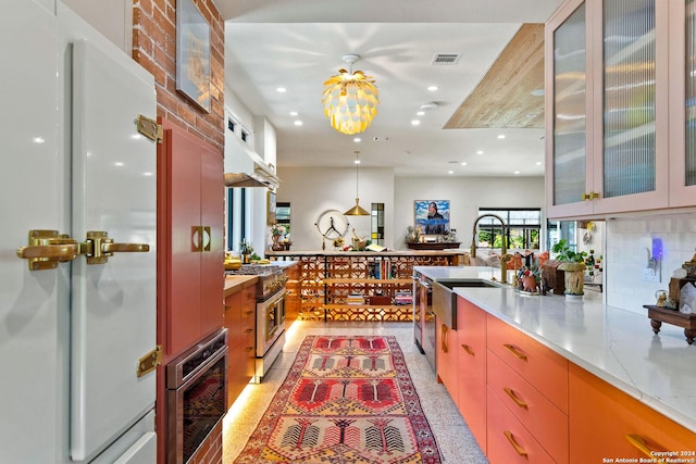 kitchen with stainless steel appliances, sink, stainless steel counters, backsplash, and wall chimney range hood