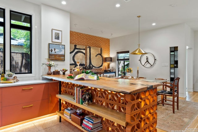 kitchen featuring hanging light fixtures, wooden counters, plenty of natural light, and brick wall