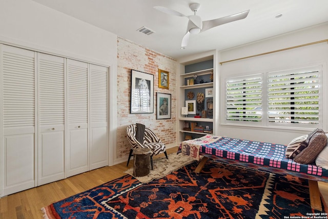 home office featuring brick wall, built in shelves, ceiling fan, and wood-type flooring