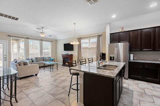 kitchen with sink, a kitchen breakfast bar, stainless steel fridge with ice dispenser, light stone countertops, and a kitchen island with sink