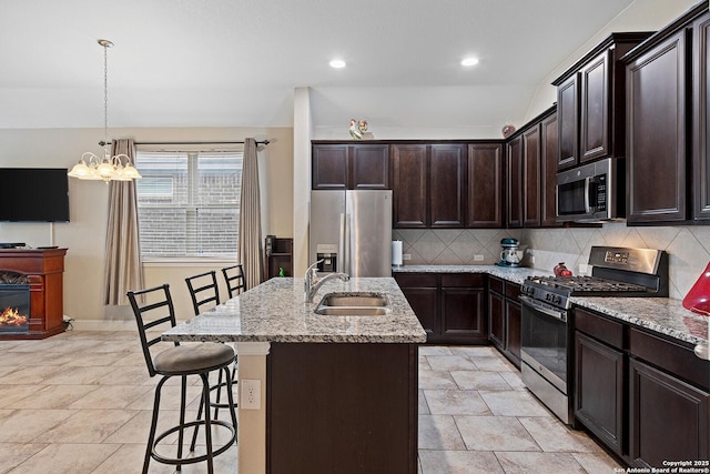 kitchen with light stone counters, appliances with stainless steel finishes, a kitchen island with sink, and sink