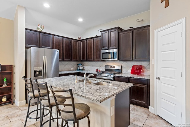 kitchen with light stone counters, stainless steel appliances, a center island with sink, a kitchen bar, and sink