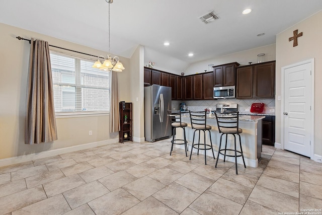 kitchen with an inviting chandelier, a kitchen breakfast bar, an island with sink, decorative backsplash, and appliances with stainless steel finishes