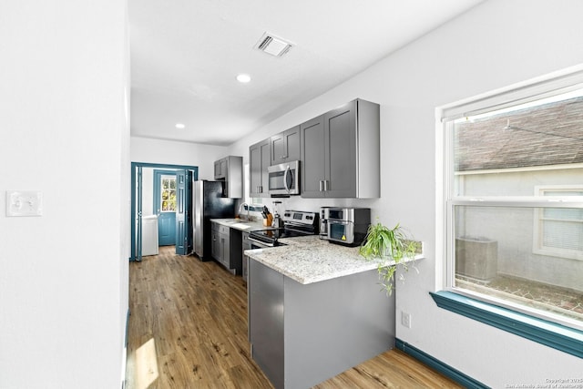 kitchen featuring light stone countertops, light wood-type flooring, gray cabinetry, appliances with stainless steel finishes, and sink