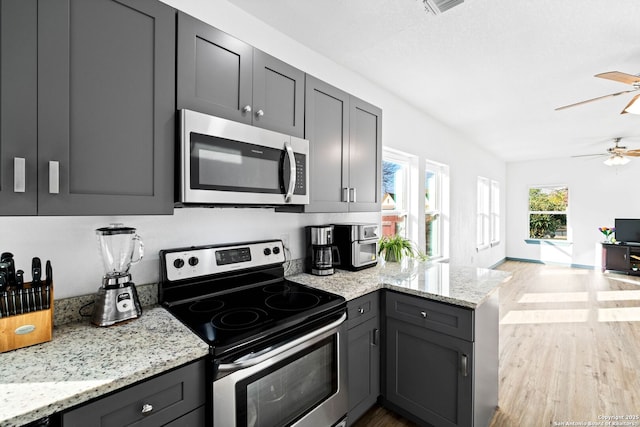 kitchen featuring light stone counters, light hardwood / wood-style flooring, gray cabinets, appliances with stainless steel finishes, and ceiling fan